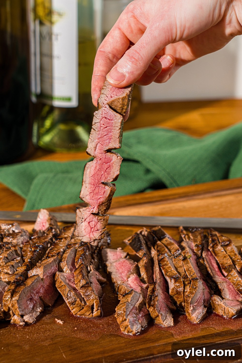London Broil Marinade Recipe for Tender, Flavorful Steak 13 A wooden board with sliced London broil served with garlic and rosemary. A hand is holding a slice of beef.