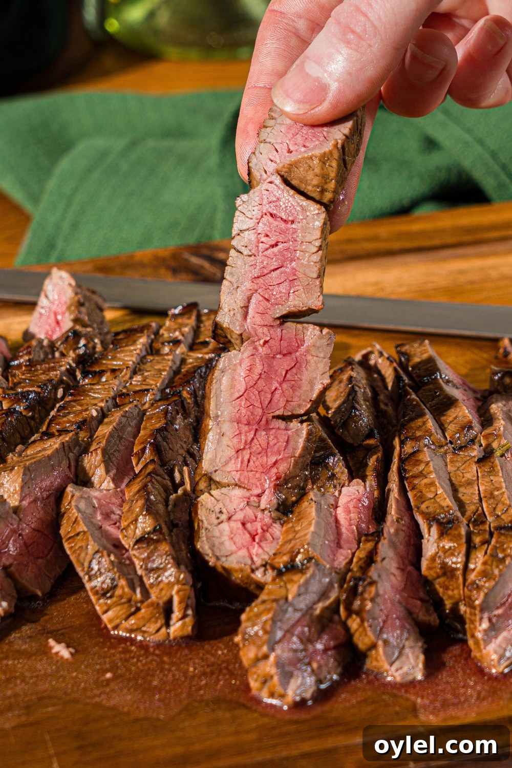 London Broil Marinade Recipe for Tender, Flavorful Steak 3 A wooden board with sliced London broil served with garlic and rosemary. A hand is holding a slice of beef.