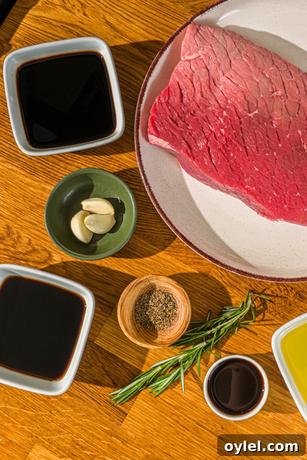 London Broil Marinade Recipe for Tender, Flavorful Steak 4 A wooden counter with several bowls in various sizes containing ingredients to make London broil marinade including London broil beef, soy sauce, balsamic vinegar, red wine vinegar, Worcestershire sauce, garlic, rosemary, and black pepper.