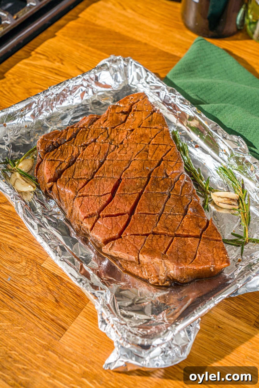 London Broil Marinade Recipe for Tender, Flavorful Steak 8 A baking sheet lined with foil with marinated London broil beef with garlic and rosemary. The sheet is on a wooden counter.