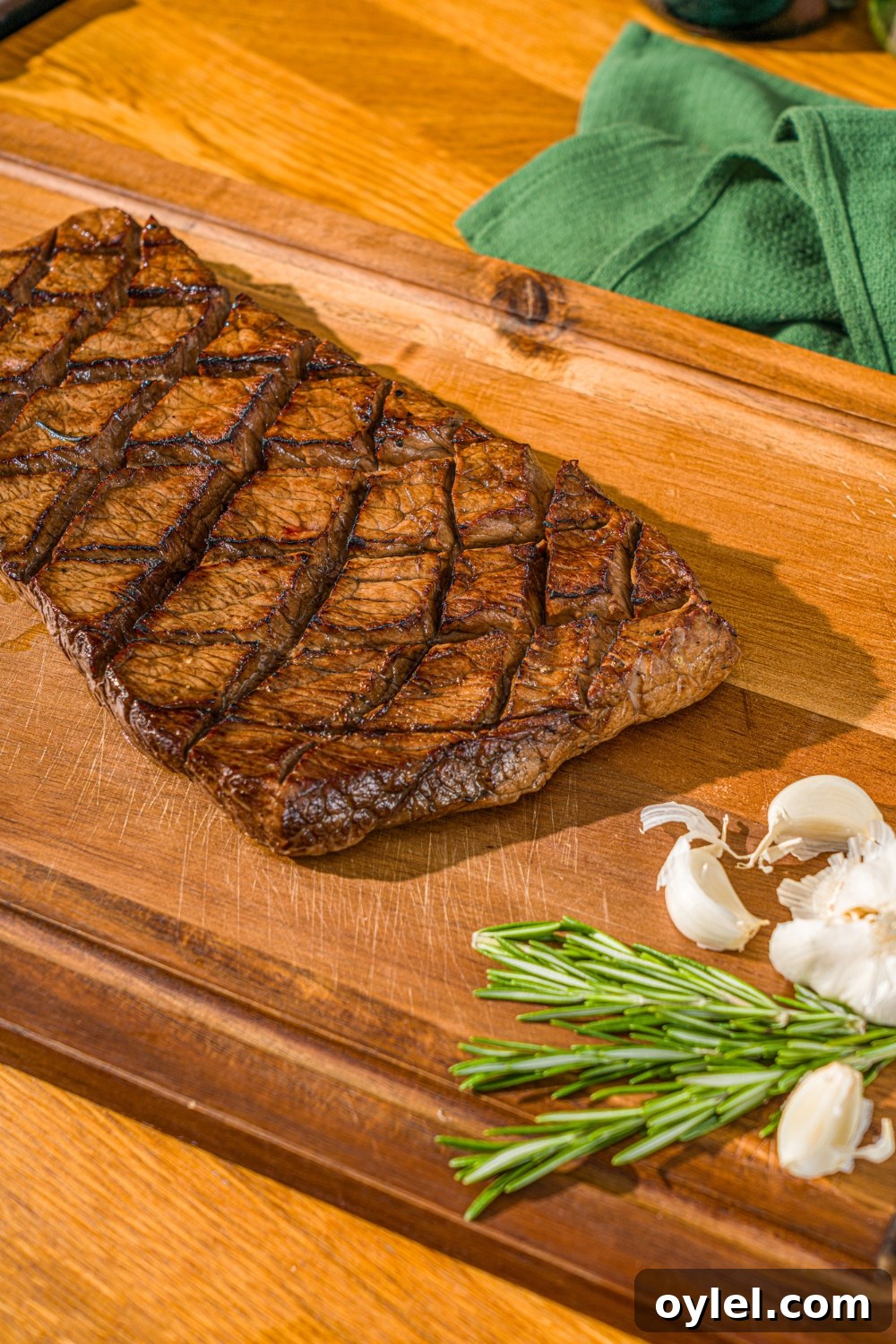 London Broil Marinade Recipe for Tender, Flavorful Steak 9 A wooden cutting board with a marinated and grilled London broil. The board is served with garlic and fresh rosemary.