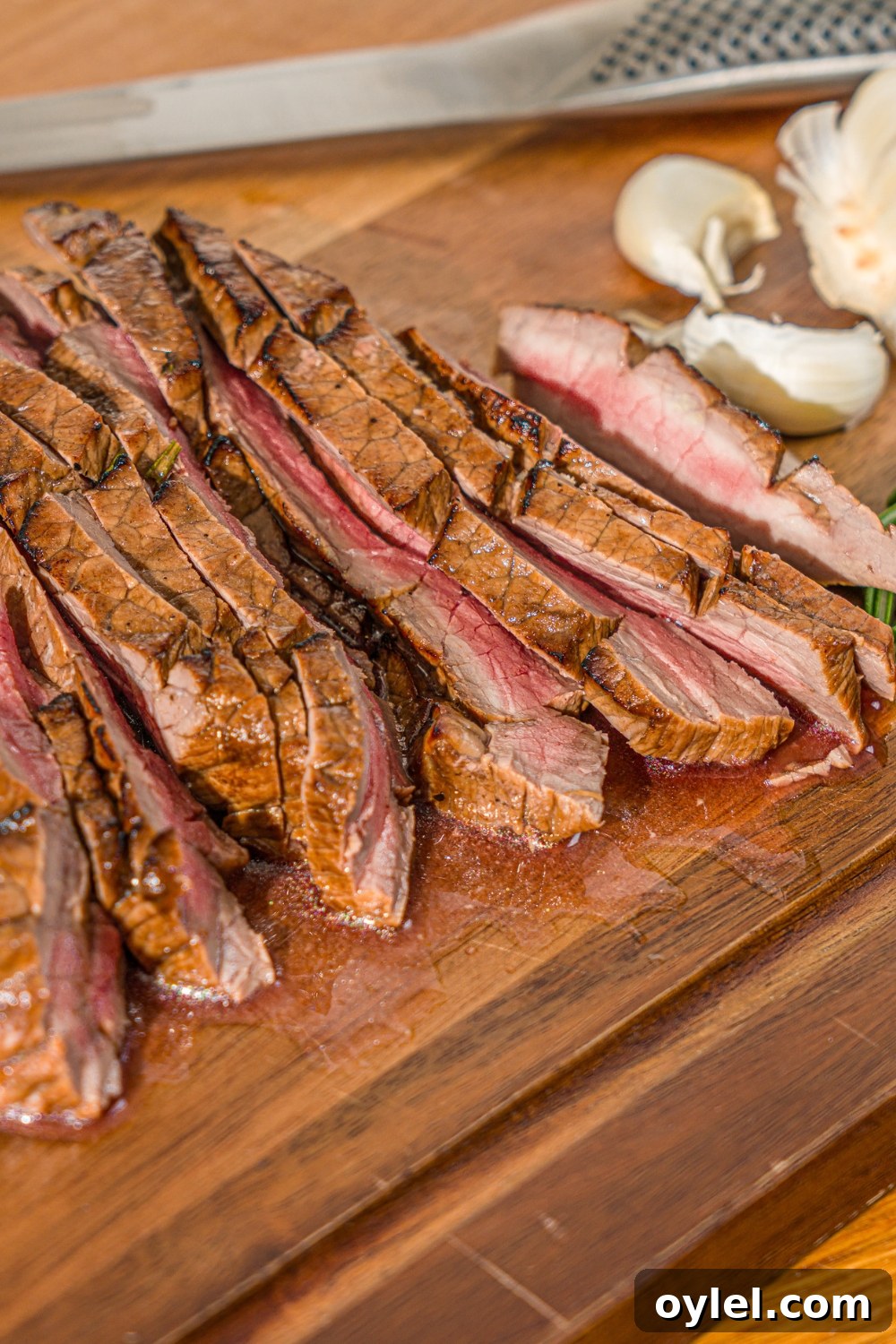 London Broil Marinade Recipe for Tender, Flavorful Steak 10 A wooden board with sliced London broil served with garlic and rosemary. There is a knife on the board.
