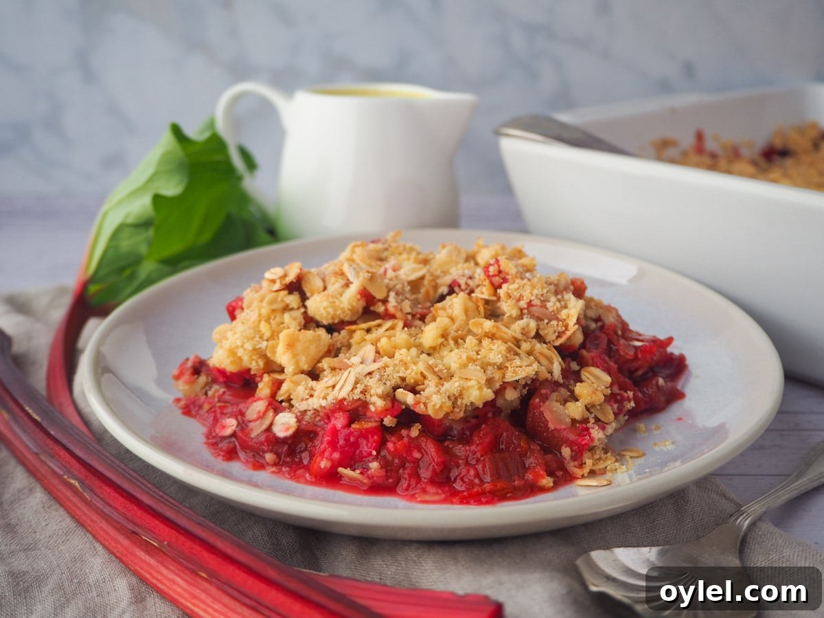 Classic Rhubarb Crumble Recipe 2 Serving rhubarb crumble with fresh rhubarb, vintage spoon, jug of custard and baking dish of crumble on the side.