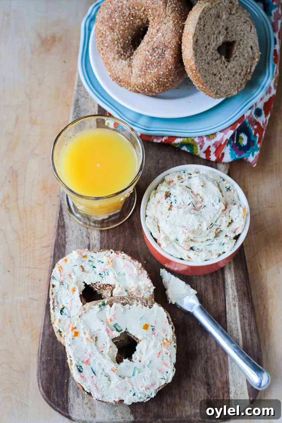 Plate of bagels next to a glass or orange juice and two bagel halves with veggie spread.
