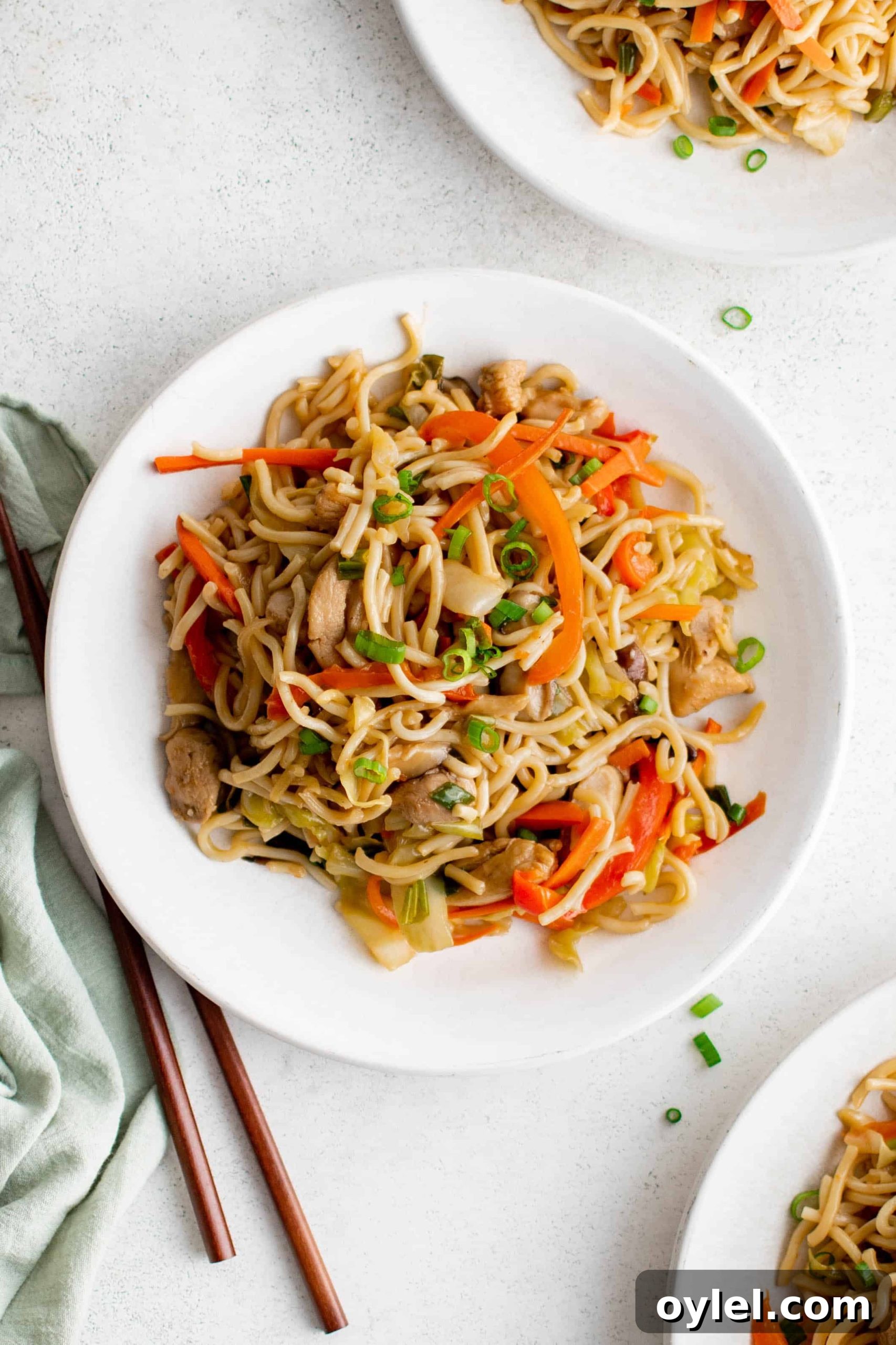 White plate filled with yakisoba noodles filled with vegetables and chicken.