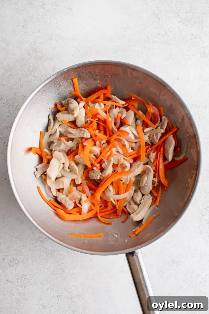 Sauteed onions, carrots, bell peppers, and chicken cooking in a large wok.