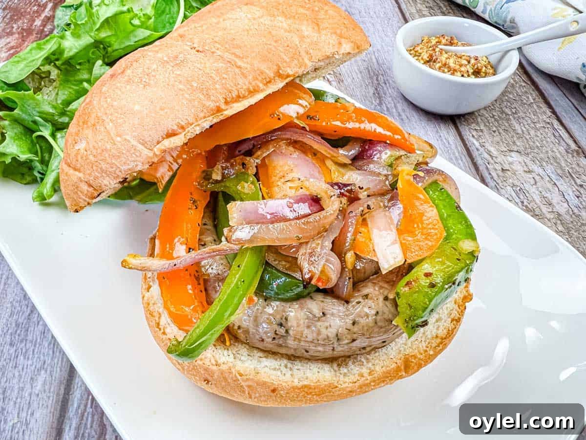 A sandwich with grilled sausage & peppers, and onions on a plate.