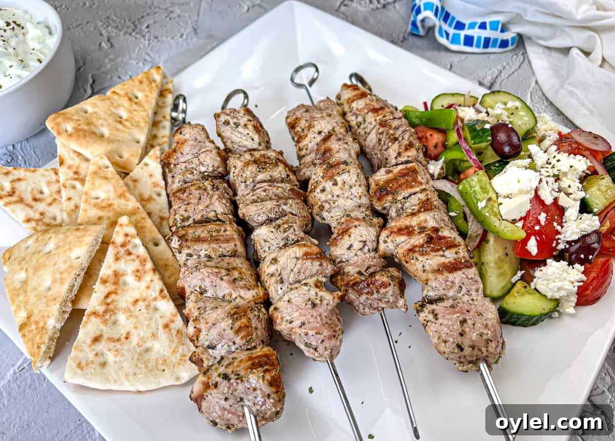Ninja Woodfire Pork Souvlaki with Horiatiki Salad and pita bread on a white plate.