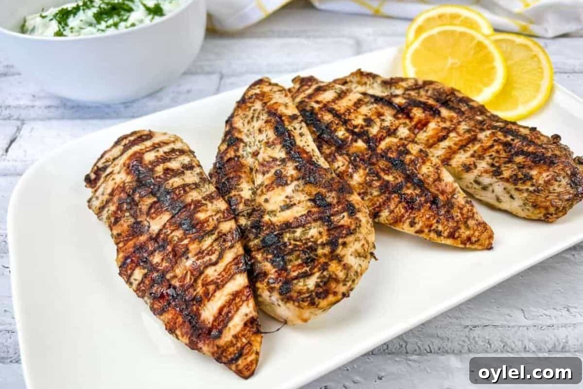 Grilled Greek Chicken on a white plate with lemon slices.
