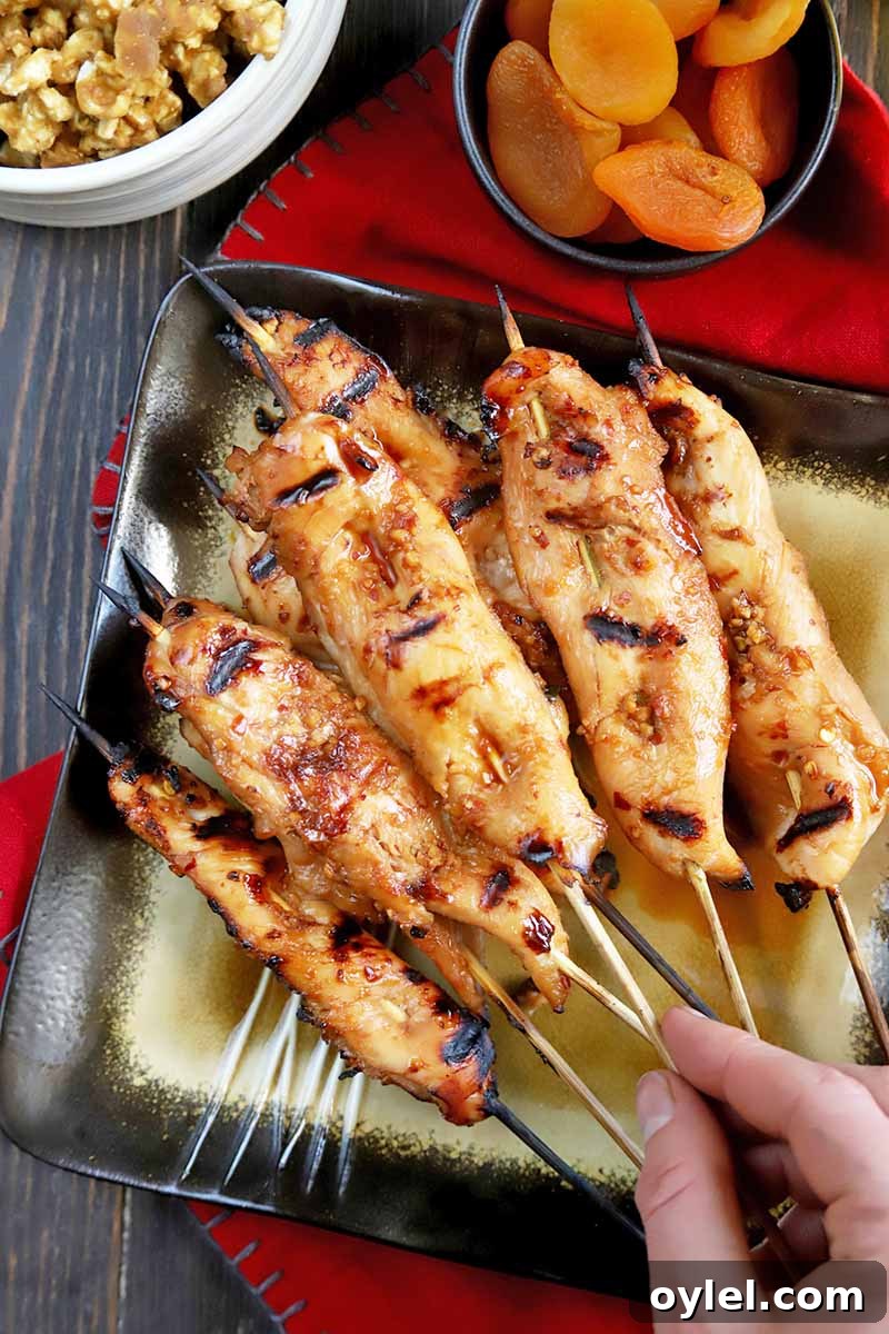 Hand reaching for a piece of grilled chicken on a skewer from a serving platter