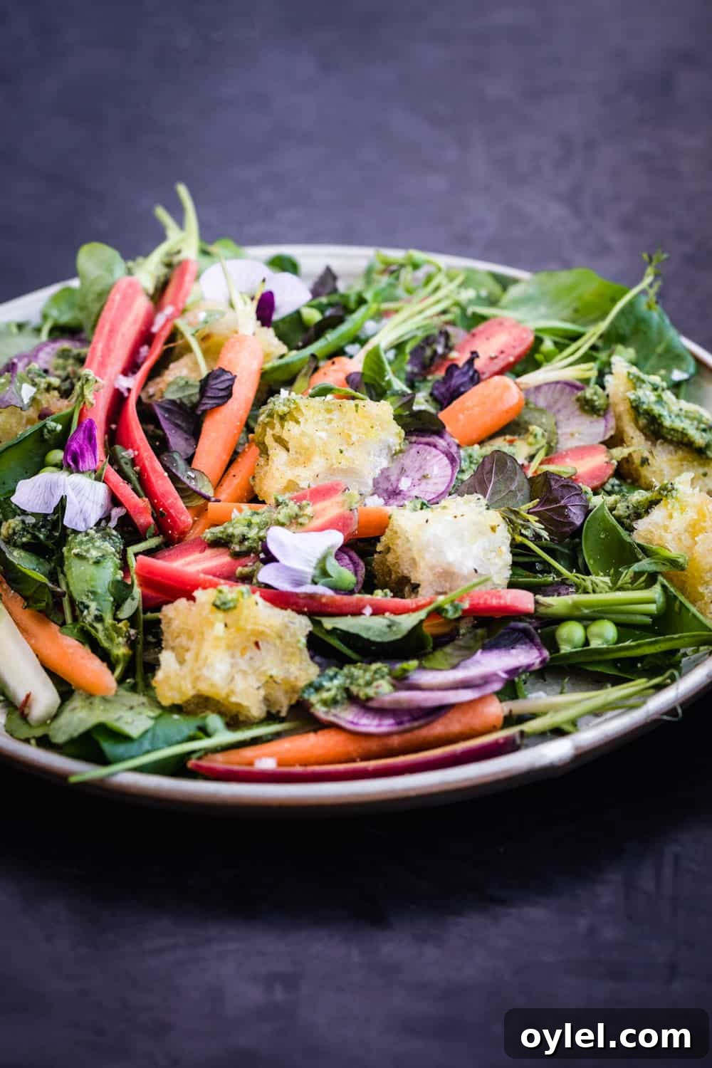 Spring Pea and Carrot Salad with Carrot Top Pesto 10 Side angle shot of the spring salad with carrot top pesto, snap peas and garlic croutons, with edible flowers and herbs.