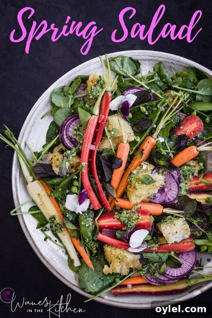 Spring salad with carrot top pesto, snap peas, garlic croutons, edible flowers and herbs on a white plate.