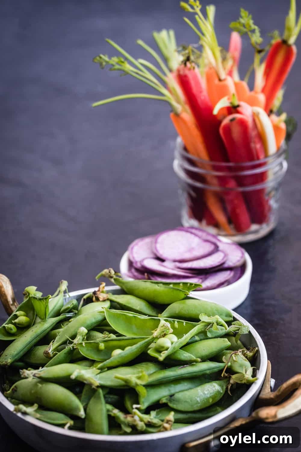 Spring Pea and Carrot Salad with Carrot Top Pesto 2 Side angle ingredient shot of snap peas, thinly sliced radishes, and thinly sliced baby carrots.