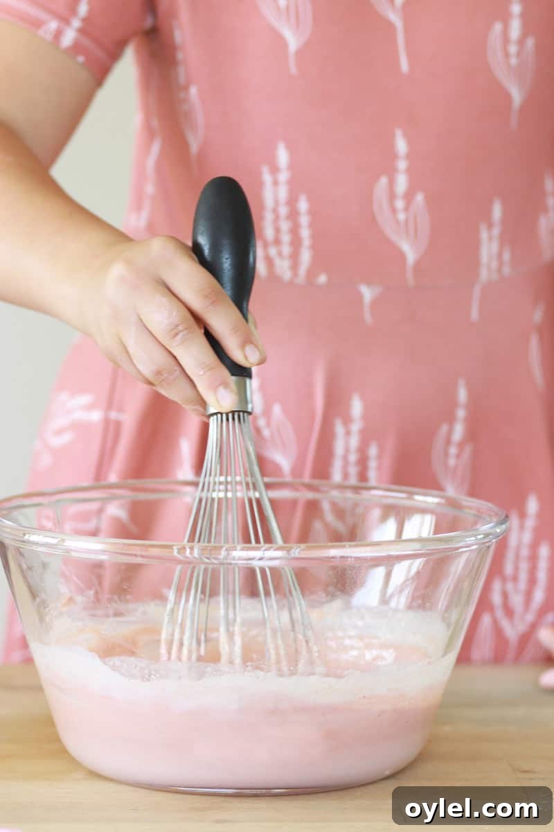 a girl in a pink dress whisks a bowl of melted soap mixture in a glass bowl