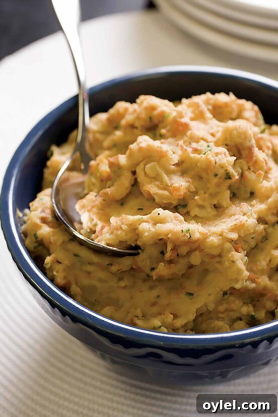 A blue bowl filled with mashed potatoes and root vegetables with a spoon resting inside.