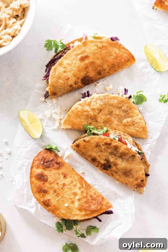 Four crispy mashed potato tacos on a sheet of white paper with a couple lime wedges on the side.