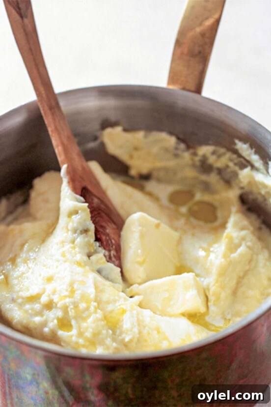 A pot of smooth mashed potatoes--made with plenty of butter, cream--with a wooden spoon and pat of butter on top
