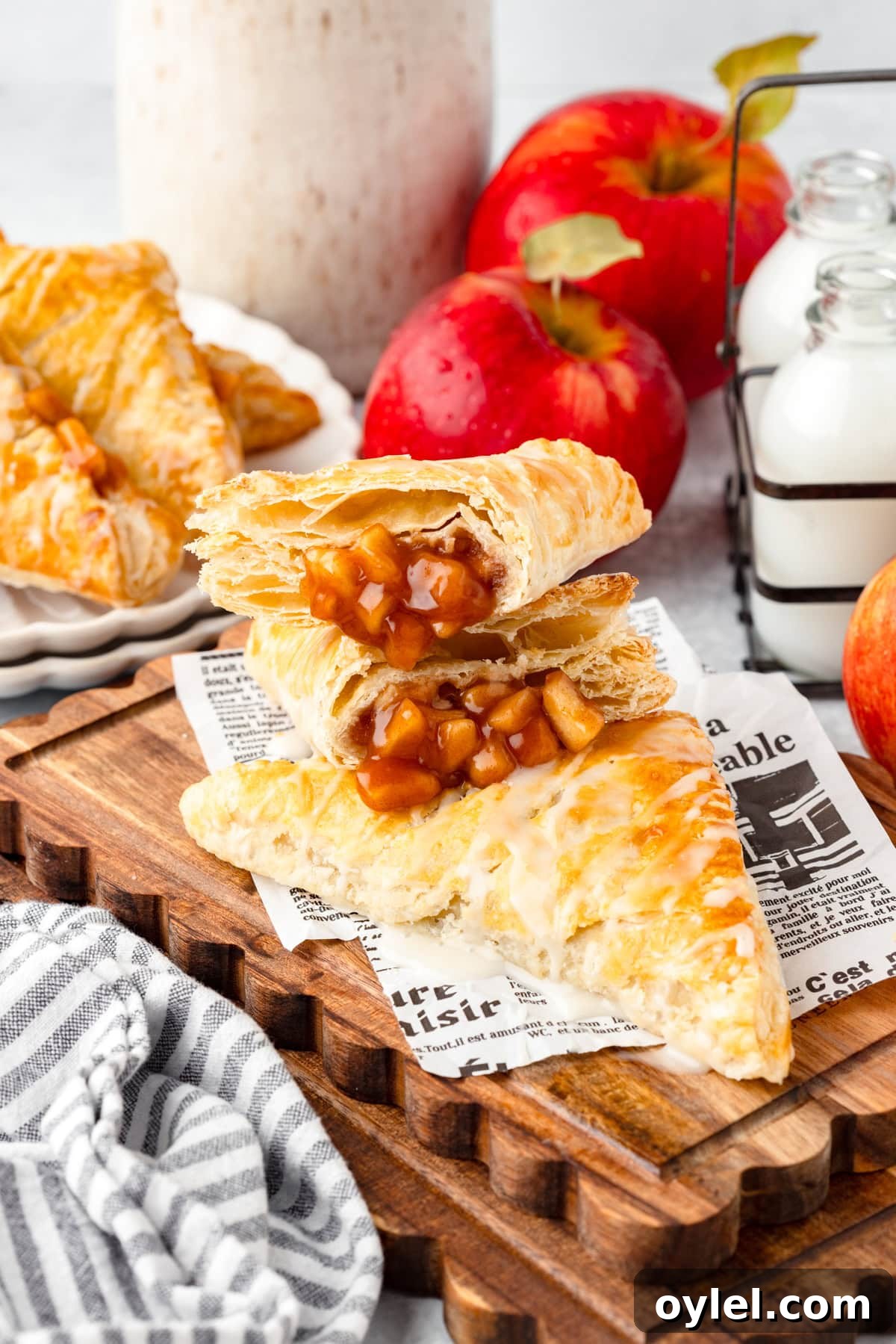 Flaky Puff Pastry Apple Turnovers Recipe 2 Stacked apple turnovers with golden, flaky pastry and sweet filling on a wooden board.