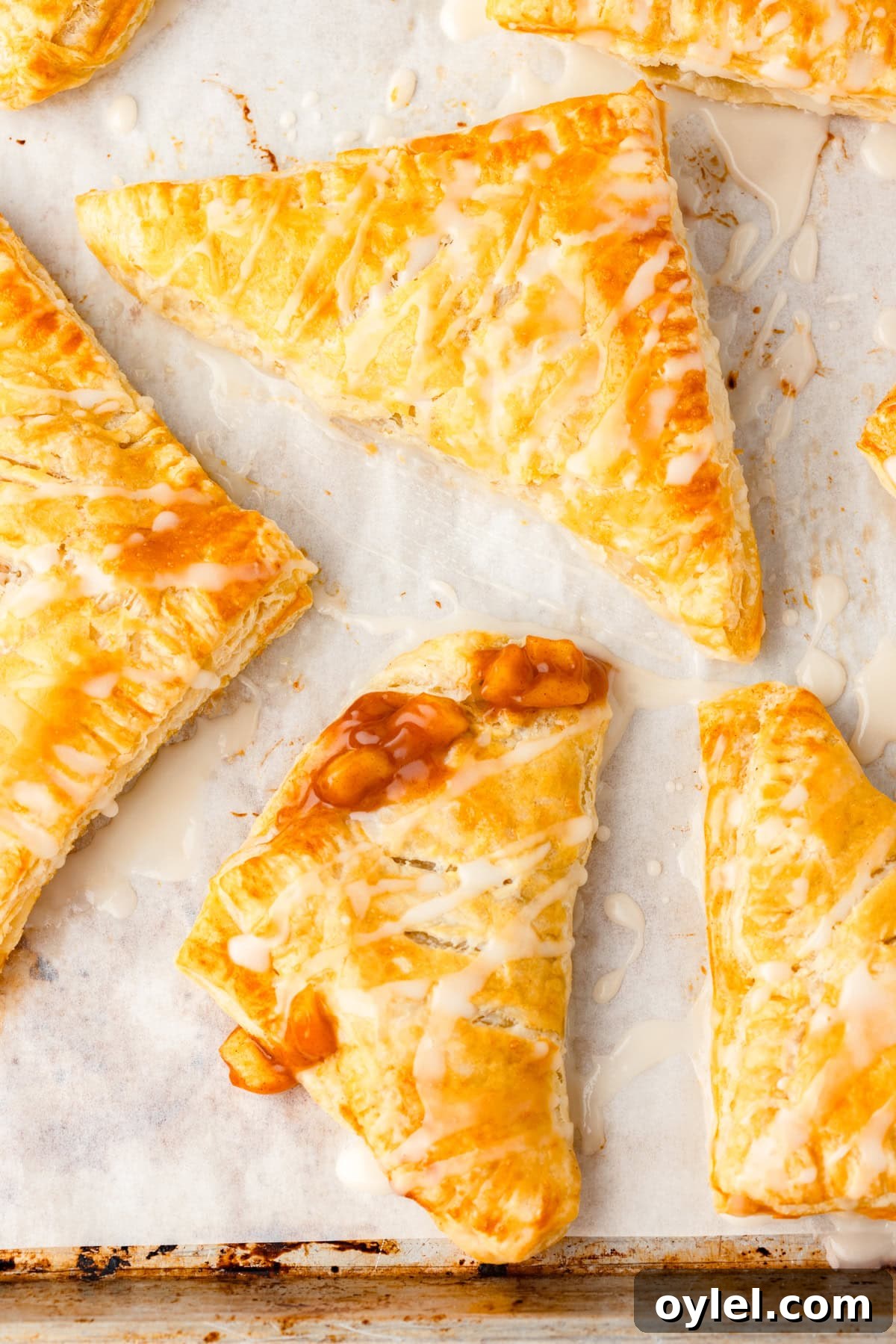Flaky Puff Pastry Apple Turnovers Recipe 5 Apple turnovers with icing on parchment paper, one showing apple filling.