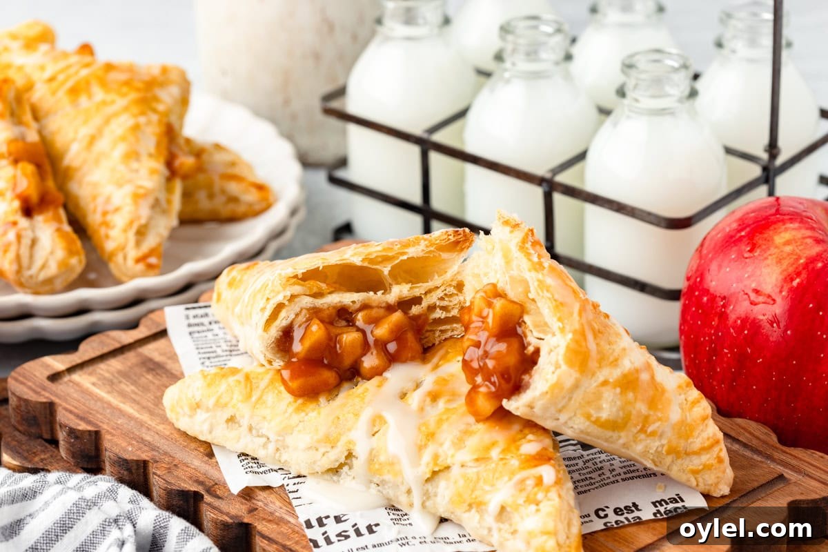 Flaky Puff Pastry Apple Turnovers Recipe 6 Golden apple turnovers on a wooden board, with a red apple and milk bottles beside them.