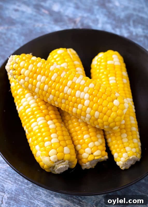 4 cobs of corn on a black plate sitting on a wooden table.