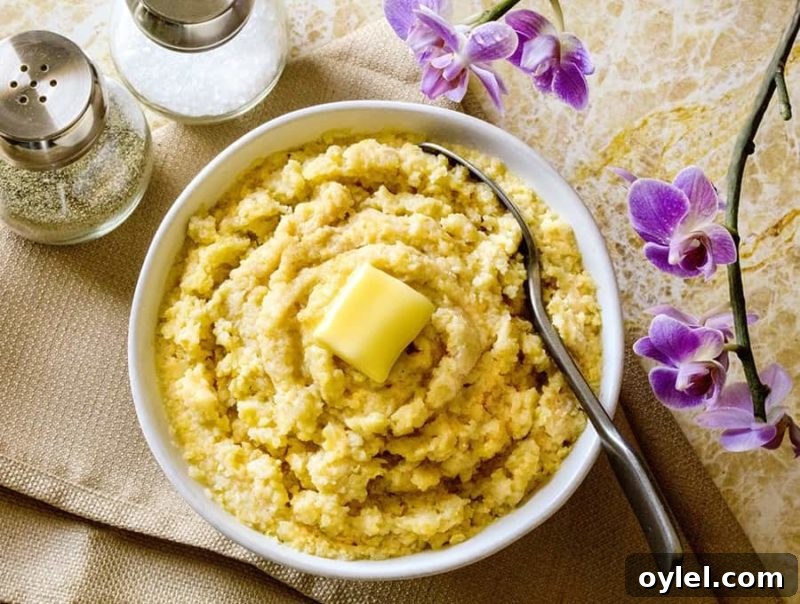 White bowl of polenta topped with butter, spoon in bowl.