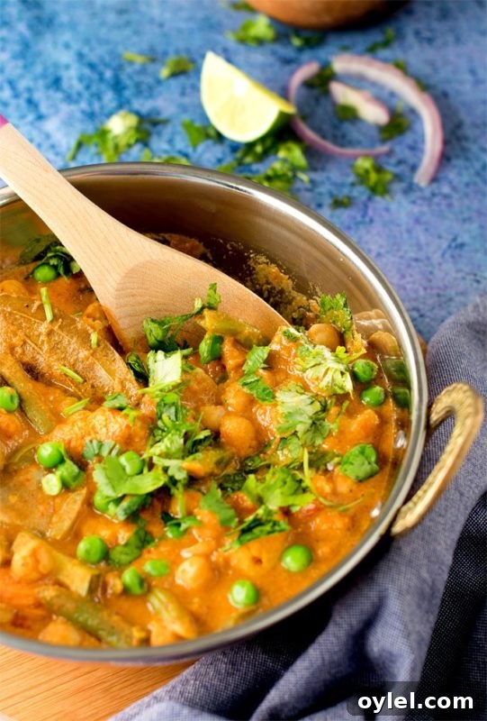 Silver bowl filled with Chickpeas and Vegetable Korma, topped with scallions and cilantro.
