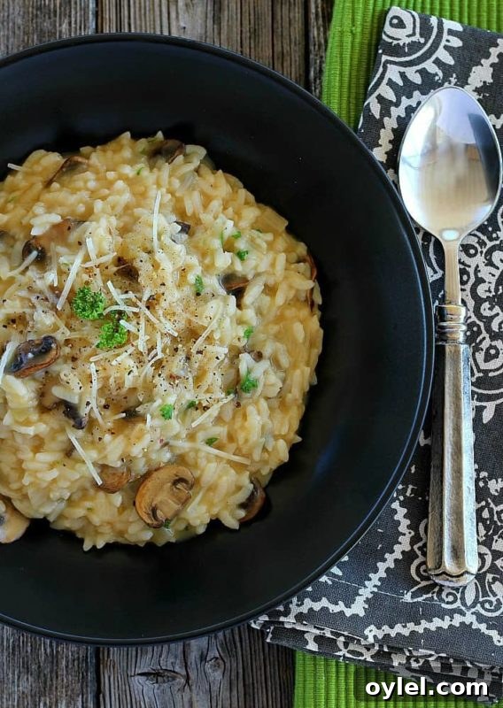 Mushroom risotto in a black bowl topped with mushrooms, scallions and Parmesan cheese, spoon on table.