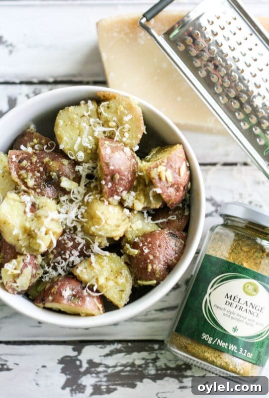 White bowl containing potato salad topped with Parmesan Cheese and Melange De France, grater and Parmesan cheese on white table.