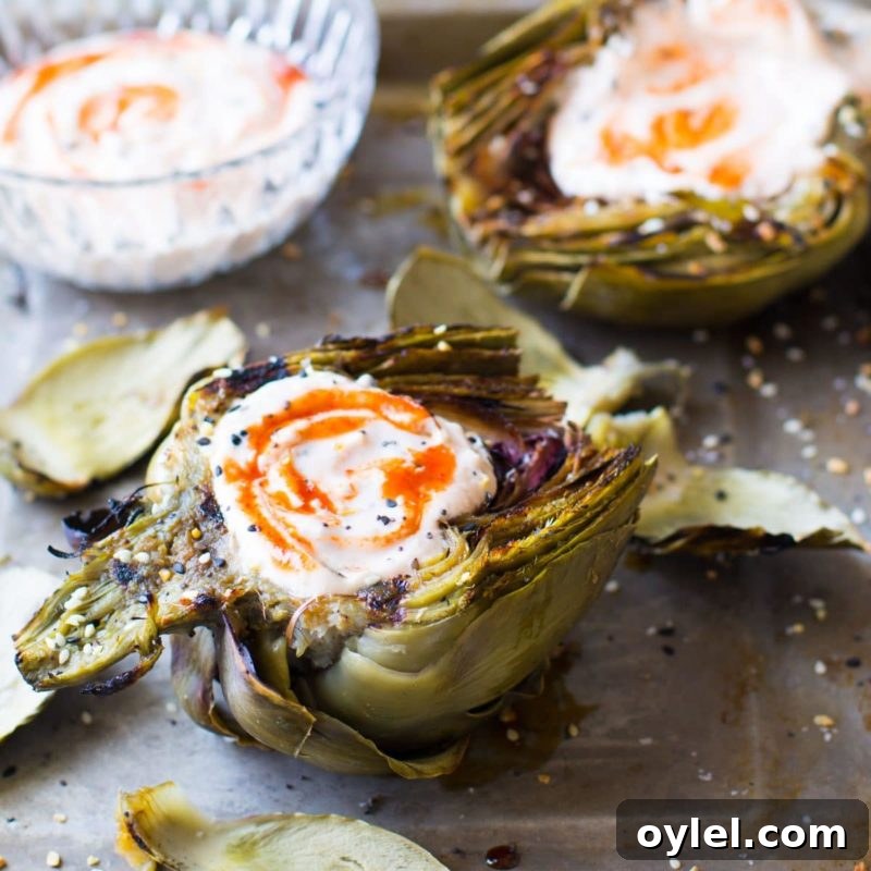 Grilled Artichokes topped with a Sriracha Dipping Sauce on a countertop, dipping sauce on side.