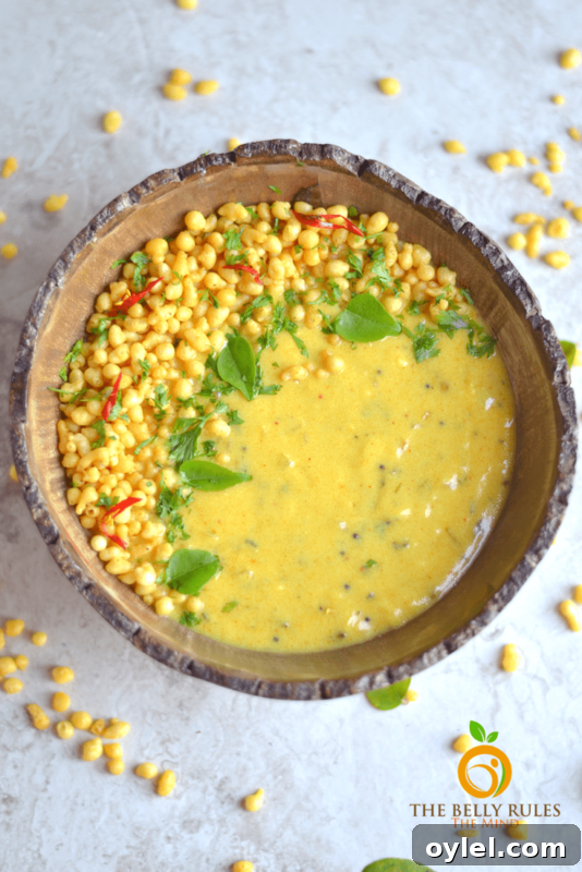 Brown bowl containing Punjabi Kadhi Pakoda, kernels of corn on table.