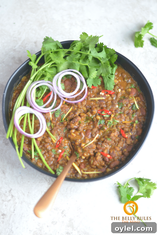 Instant Pot Dal Makhani black and kidney bean mix in a black bowl topped with onions and cilantro.