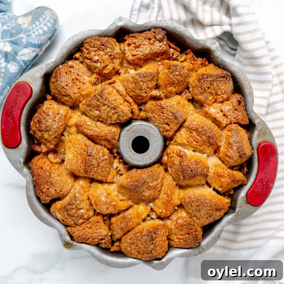 Cinnamon Pull Apart Monkey Bread with Biscuits 10 A bundt pan filled with baked monkey bread, featuring golden-brown biscuit pieces and a striped kitchen towel nearby.