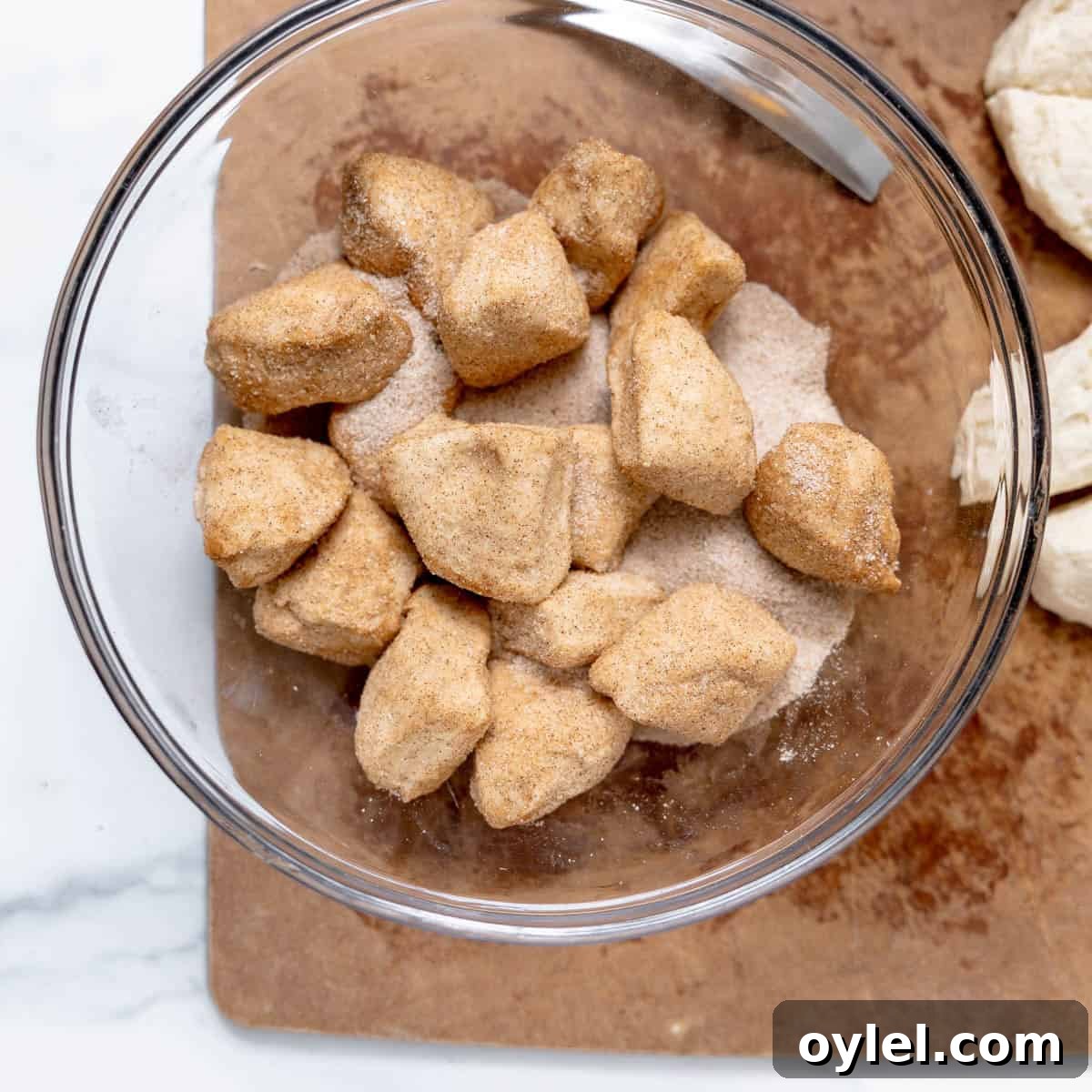 Cinnamon Pull Apart Monkey Bread with Biscuits 6 Dough pieces coated in cinnamon sugar sit in a clear glass bowl on a wooden surface.