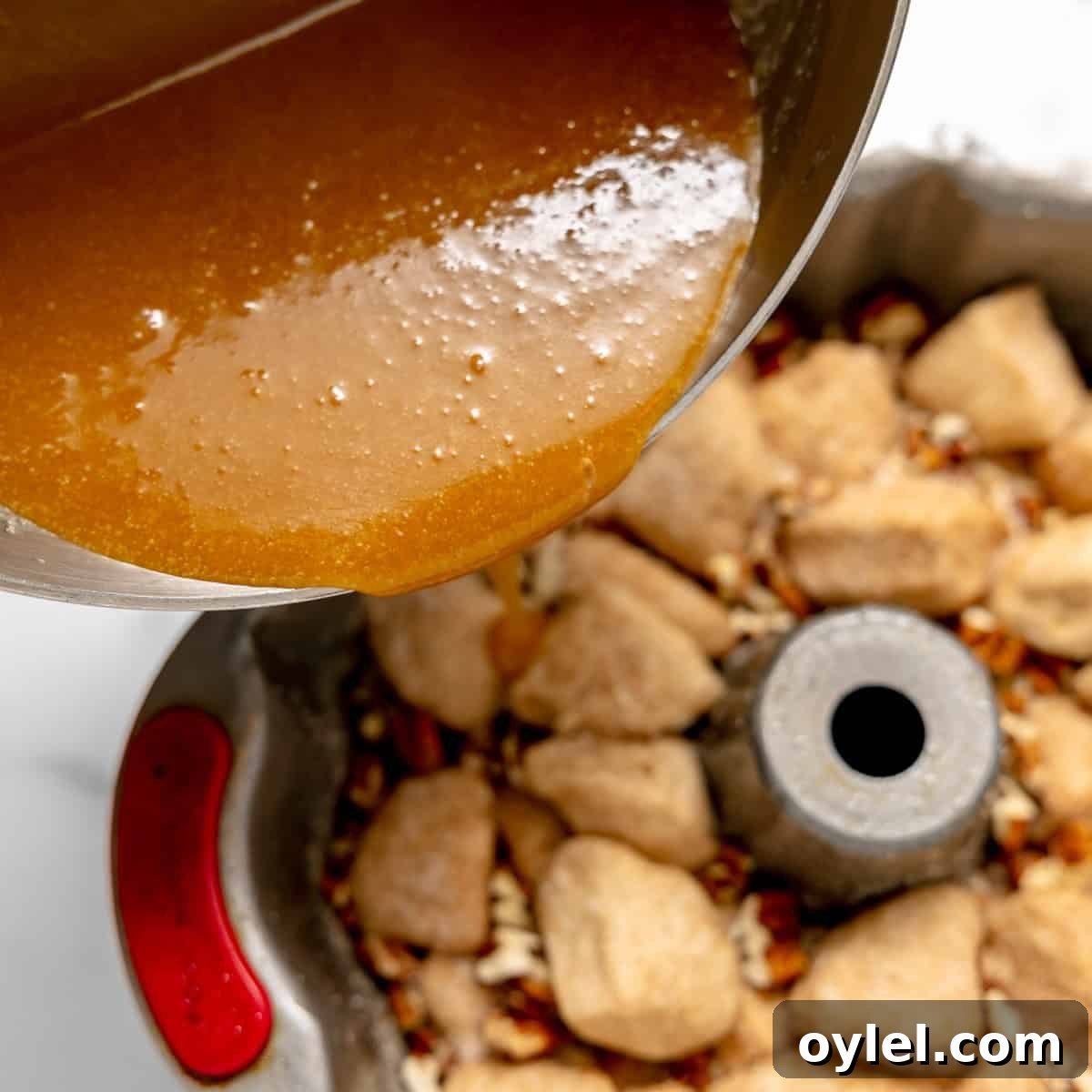 Cinnamon Pull Apart Monkey Bread with Biscuits 9 A thick caramel sauce is being poured from a saucepan over biscuit dough pieces and chopped pecans in a bundt pan.