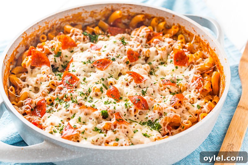 Pan filled with pizza pasta sitting on top of a blue napkin with a wooden spoon resting next to it.