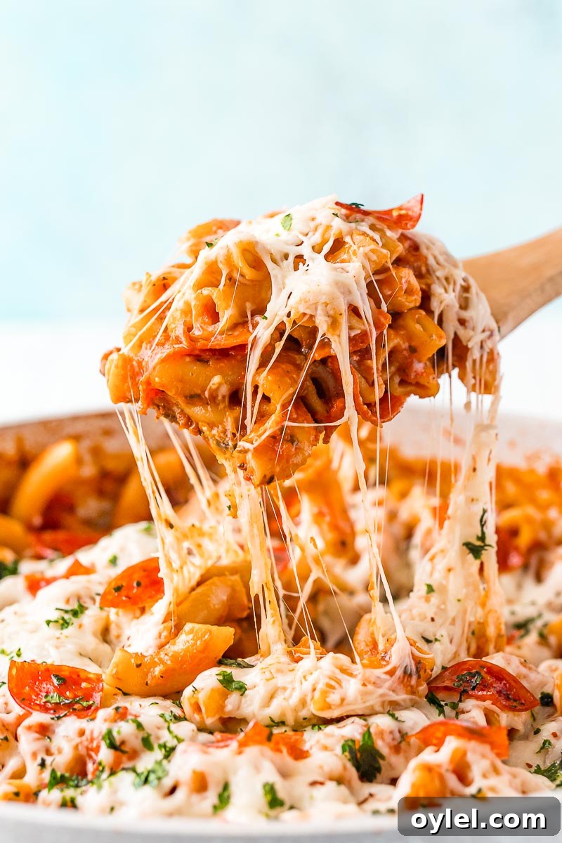 A scoop of pizza pasta being lifted from the pan. Cheese is stretching from the spoon to the pan.